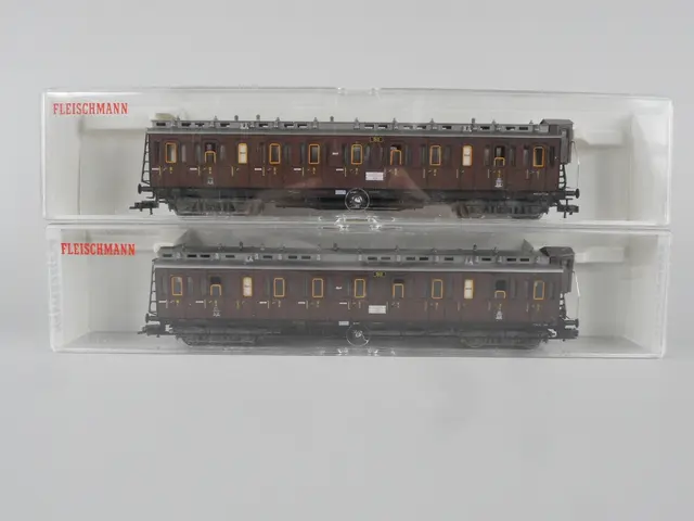 The image shows two model train cars in a clear box on a white background. The cars are brown in...