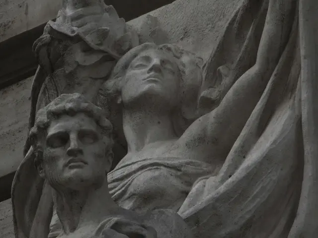 The image shows a statue of two women on the side of a building, with a wall in the background. The...