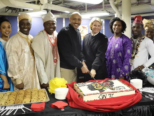 The image shows a group of people standing around a table with a cake, plates, bowls, spoons,...