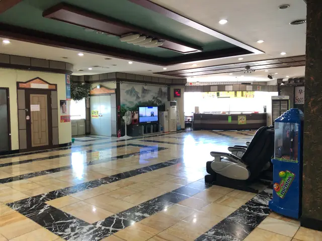 The image shows the lobby of a hotel with a large marble floor, electric lights to the roof, doors,...