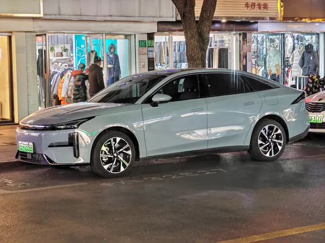 The image shows an electric car parked on the side of a street at night, surrounded by buildings,...
