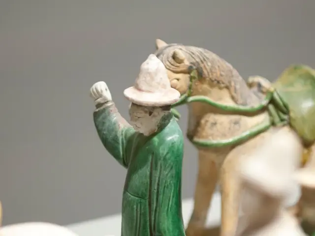 The image shows a group of Chinese terracotta figurines on display in a museum, with a person and a...