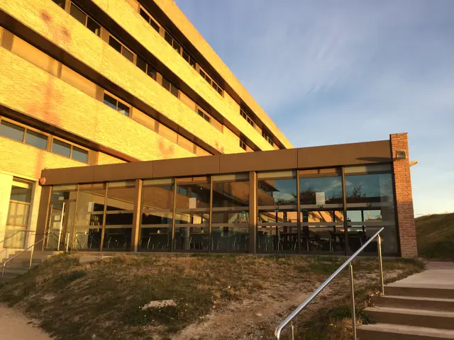 The image shows a large building with a lot of windows and stairs leading up to it, surrounded by...