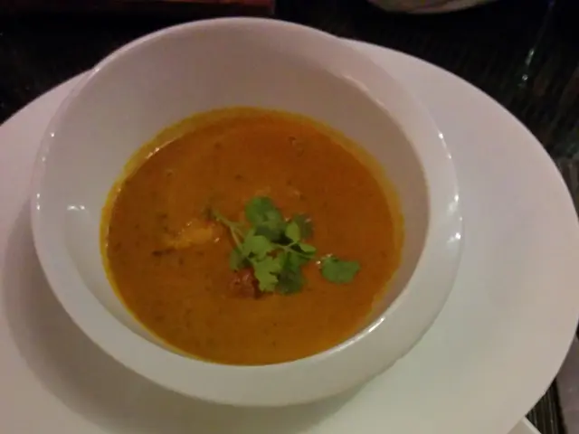 The image shows a white plate topped with a bowl of curry and rice, accompanied by a plate of naan...