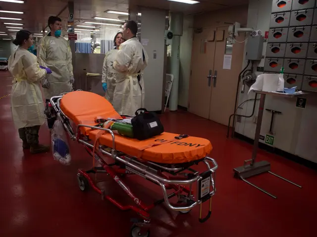 The image shows a group of people in protective gear standing around a gurney in a hospital room....
