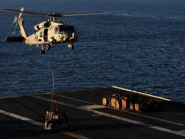The image shows a helicopter flying over the ocean with a rope attached to it. On the deck of the...