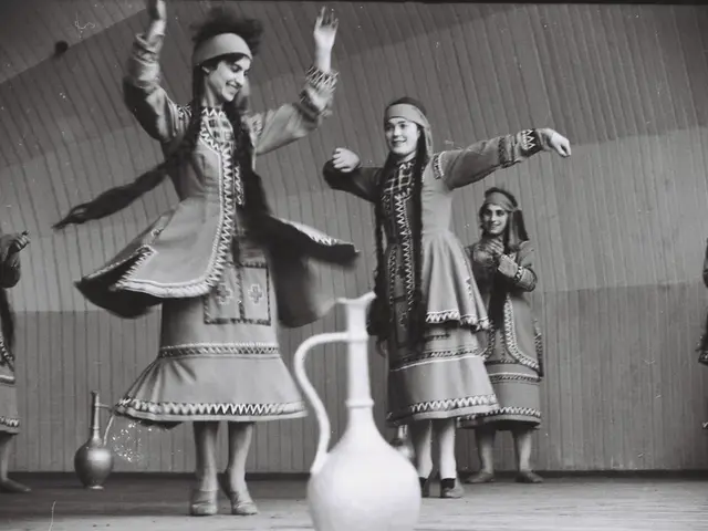 The image shows a group of women in traditional Greek dress dancing on a stage, with a jug in the...