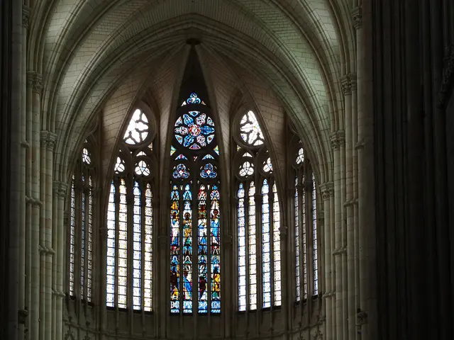 The image shows a large stained glass window in a cathedral with a vaulted ceiling and pillars on...