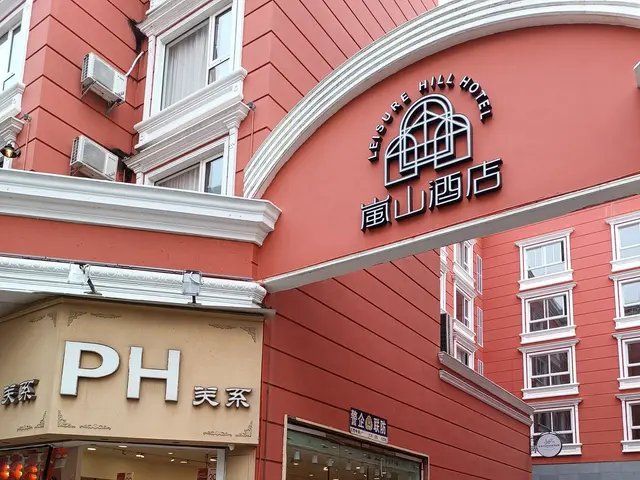 The image shows a group of people walking down a street in front of a building with windows, air...