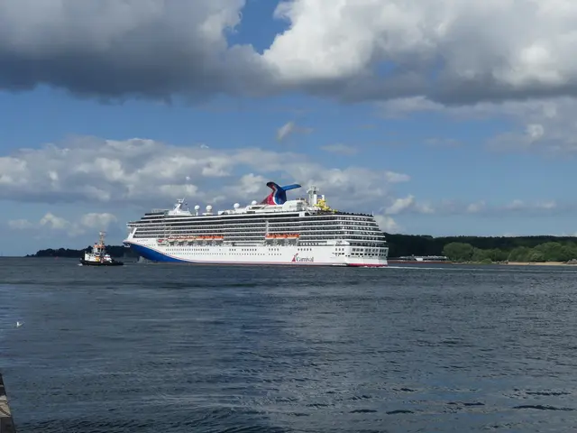 The image shows a Carnival cruise ship docked at a dock in the water, surrounded by a few boats. On...