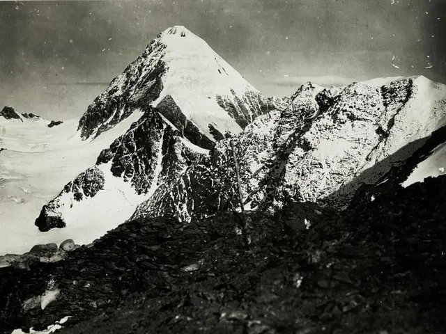 The image shows a black and white photo of a snow-covered mountain, with the sky in the background....