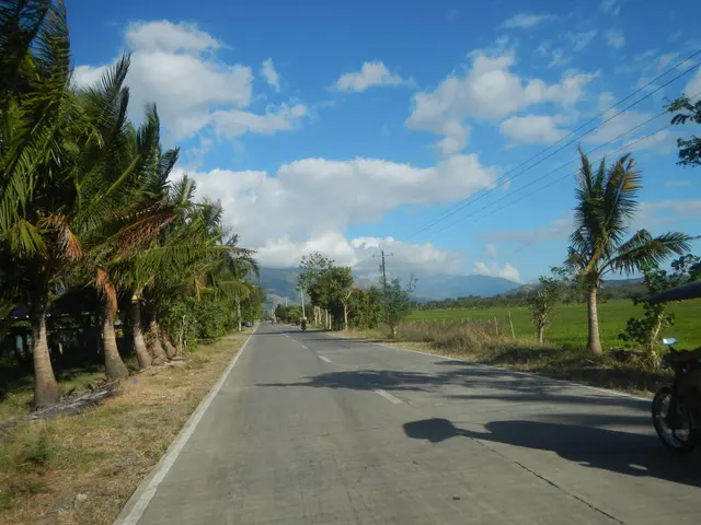 The image shows a road with a motorcycle parked on the side of it, surrounded by lush green grass...