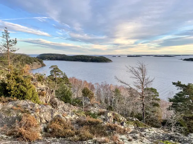 The image shows a breathtaking view from the top of a hill overlooking a body of water, with trees,...