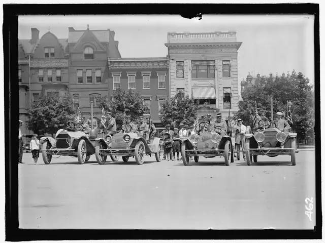 The image shows a group of people riding in vintage cars down a street, with buildings and trees in...