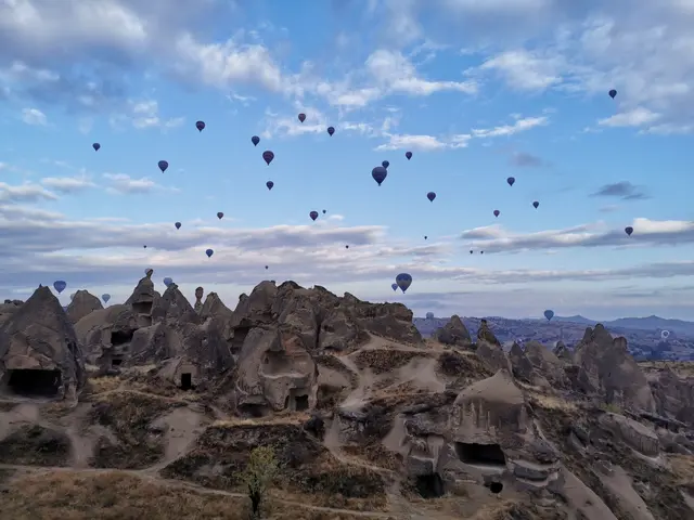 The image shows hot air balloons flying over the rocky landscape of Cappadocia, Turkey, with...