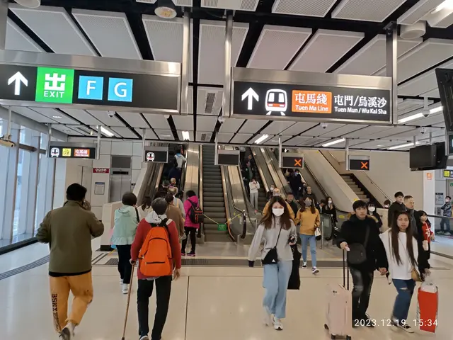 The image shows a group of people walking through an airport with luggage, some of them wearing...