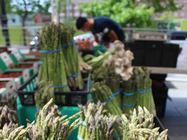 The image shows asparagus for sale at a farmers market, with a person standing in the background...