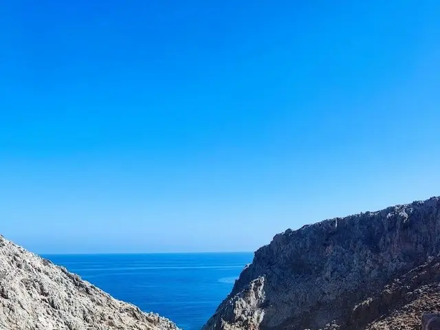 The image shows a stunning view of a beach from the top of a mountain, with the crystal clear blue...