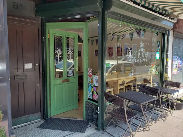 The image shows a restaurant with tables and chairs outside of it, surrounded by plants and a...