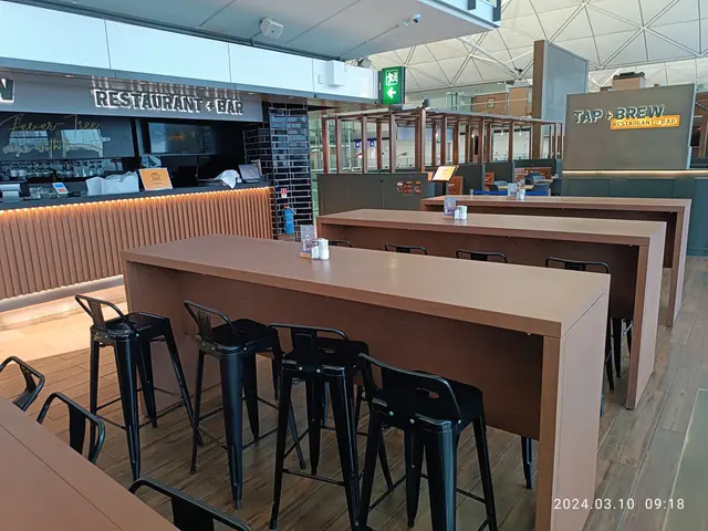 The image shows a restaurant with tables and chairs in the middle of it, surrounded by boards with...