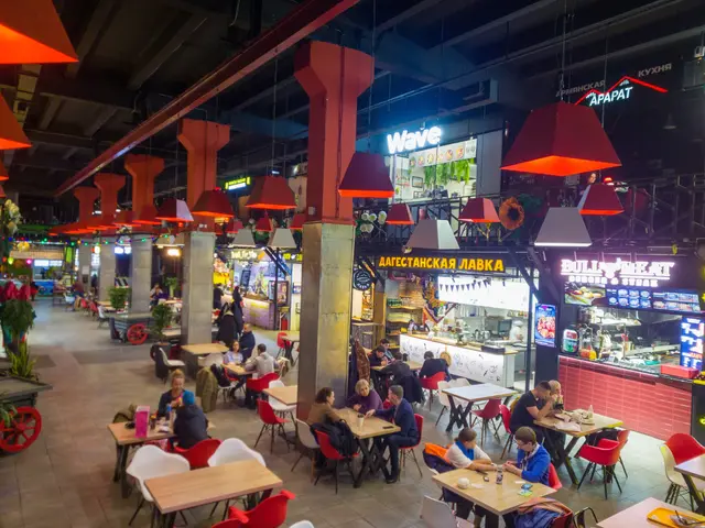 The image shows the interior of a restaurant with people sitting at tables and chairs. There are...