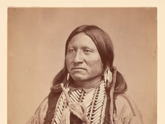 The image shows an old black and white photo of an Indian man wearing traditional clothing and...