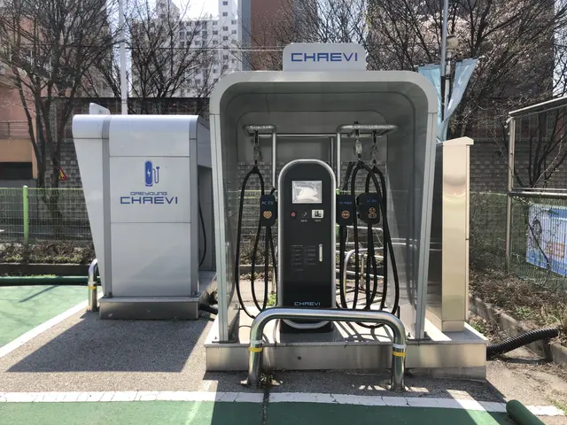 The image shows an electric vehicle charging station in the middle of a park, surrounded by a metal...