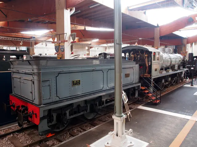 The image shows an old steam locomotive on display in a museum, surrounded by railway tracks,...