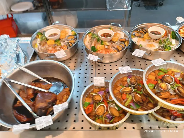 The image shows a buffet filled with lots of different types of food, including bowls of seafood,...