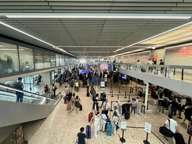 The image shows a large group of people walking through an airport, some of them carrying bags....
