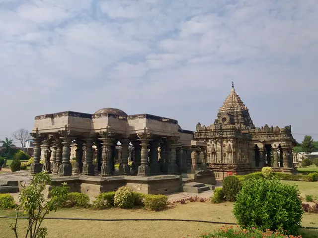 The image shows a large stone building with pillars in the middle of a park, surrounded by lush...