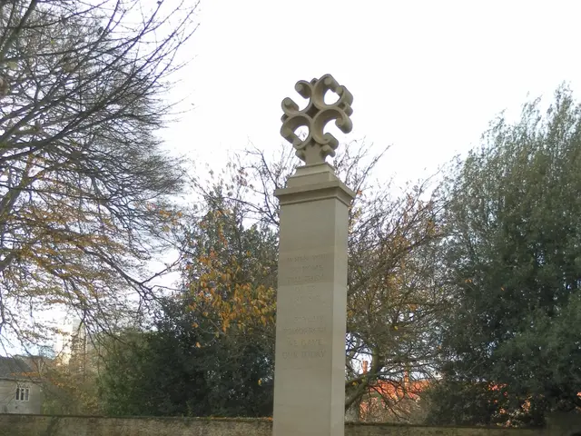 The image shows a war memorial with wreaths on it in the middle of a park, surrounded by grass and...