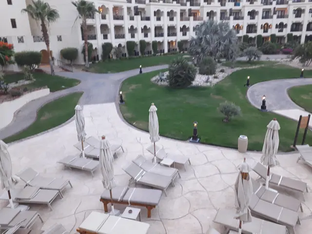 The image shows a view of a resort from the top of a building, with lounge chairs and umbrellas in...